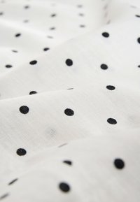 White fabric with black polka dots, showcasing a smooth texture and subtle sheen, arranged in a scattered, irregular pattern.