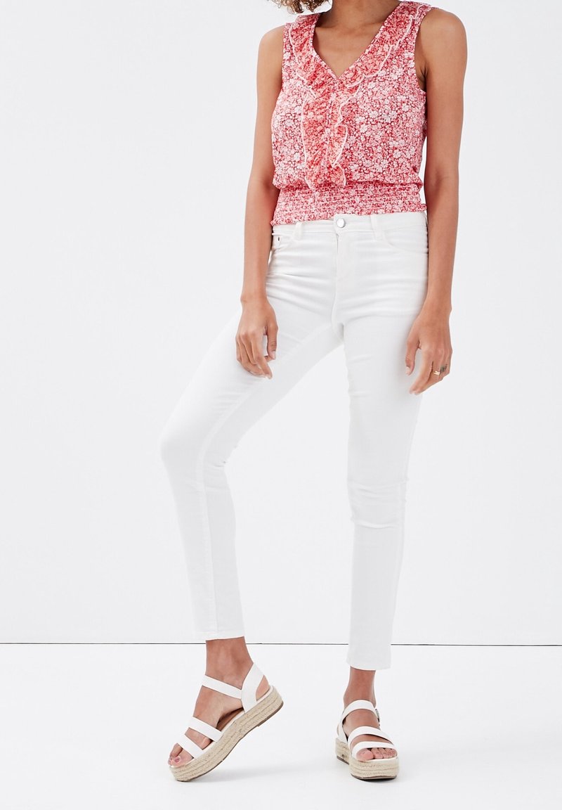 Haut sans manches rouge à motifs floraux avec encolure à volants, pantalon blanc slim et sandales espadrilles beiges avec des lanières blanches.