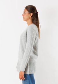 Maglione grigio a maglia con una texture a coste. Presenta maniche lunghe, un collo rotondo e una vestibilità leggermente over size.