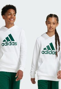 Sudaderas blancas con un gran logo verde de Adidas, que cuentan con bolsillos de canguro y puños acanalados, combinadas con pantalones verdes.