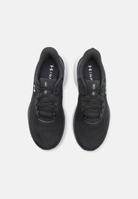 Baskets de sport noires avec une tige en mesh, bout rond et semelle rembourrée. Elles disposent de lacets noirs et d'un logo Under Armour sur le côté.