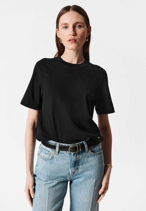 Black cotton t-shirt with short sleeves, crew neck, relaxed fit. Paired with light blue denim jeans and a black belt featuring a gold buckle.