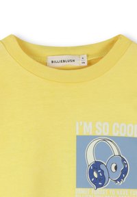 T-shirt jaune avec un graphisme de casques audio en forme de beignets et le texte "JE SUIS TELLEMENT COOL" au-dessus et "N'OUBLIE PAS DE T'AMUSER" en dessous.
