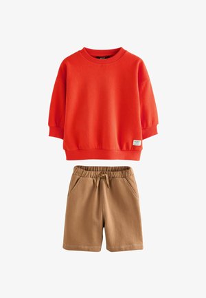 Rotes Sweatshirt mit Rundhalsausschnitt und gerippten Bündchen sowie beigen elastischen Shorts mit Kordelzug und Seitentaschen, flach auf weißem Hintergrund ausgelegt.