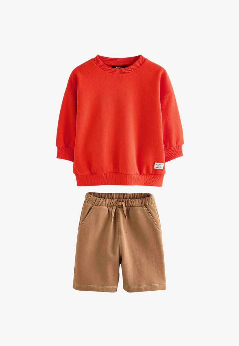Rød crewneck sweatshirt med ribbede manchetter og beige elastiske shorts med snøre og sidelommer, lagt fladt på hvid baggrund.