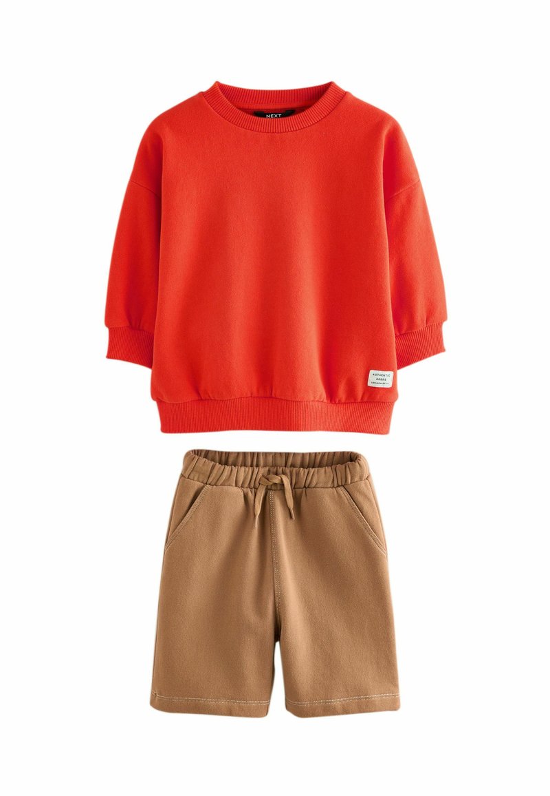 Red crewneck sweatshirt with ribbed cuffs and beige elastic waist shorts with drawstring and side pockets, laid flat on white background.