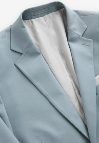 Hellblaues Blazer mit Reverskragen, strukturiertem Stoff und weißem, gemustertem Innenfutter. Enthält eine Brusttasche und dezente Nähdetails.