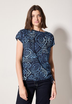 Navy blue t-shirt with geometric light blue patterns, short sleeves, and a side tie detail for adjustment. Soft fabric texture.