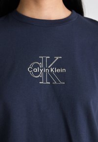 Navy blue cotton T-shirt featuring a white Calvin Klein logo with stylized letters, round neckline, and short sleeves.