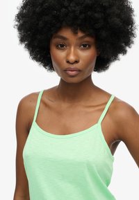 Mintgrøn tanktop med tynde stropper, lavet af et blødt, let tekstureret stof og med en afslappet pasform, der fremhæver halsudskæringen og skuldrene.