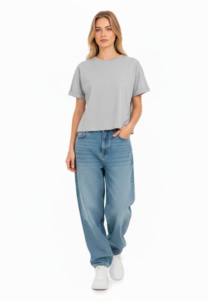 Grijze cropped t-shirt met opgerolde mouwen, gecombineerd met lichtblauwe baggy jeans. Model draagt witte sneakers. Eenvoudige, casual mode.
