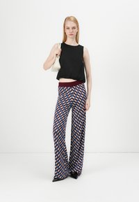 Top senza maniche nero, pantaloni a gamba larga con motivo a rombi blu, rossi e bianchi, e una piccola borsa off-white. Scarpe nere a punta.