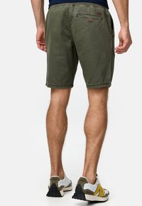 Shorts vert olive avec un design à 5 poches, ourlet cousu et une fermeture à un bouton à l'arrière. Portés avec des chaussures de sport multicolores.