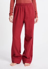 Czerwone szerokie spodnie w kratę z elastycznym pasem. Materiał ma miękką teksturę i prezentuje mały wzór siatki na całej powierzchni.