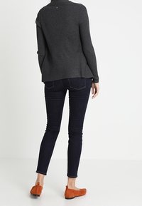 Grå ribbstickad tröja, bakifrån; matchas med mörkblå smala jeans och orangea mockaskor. Enkel design med avslappnad passform.