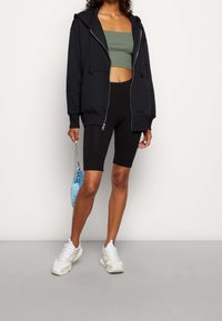 Black zip-up hoodie with drawstrings, green crop top, black bike shorts, white sneakers, and a blue mini handbag with a chain strap.