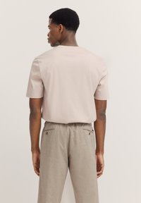 Light pink short-sleeve t-shirt with a relaxed fit, paired with beige relaxed trousers featuring button accents and side pockets.