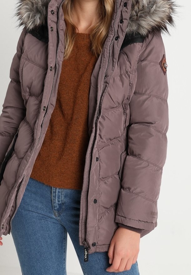 Giacca puffer viola chiaro con cappuccio in pelliccia sintetica, design trapuntato, chiusura con zip e bottone, e polsini a costine, indossata sopra un maglione marrone.