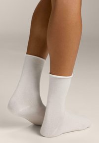 Weiße Baumwollknöchelsocken mit geripptem Bund, glatter Textur und einfachem Design. An den Füßen gezeigt, wobei der Fuß- und Knöchelbereich betont wird.