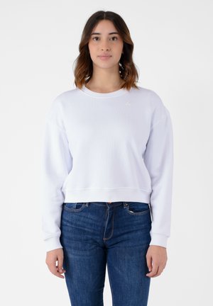 Felpa bianca croppata con scollatura e polsini a costine, caratterizzata da un piccolo logo sul petto. Abbinata a jeans in denim blu.