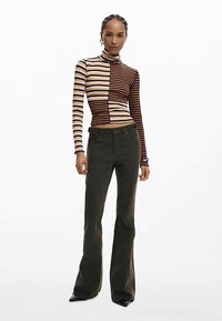 Gestreepte coltrui in bruin en crème, gecombineerd met donker groene wijde jeans. Het materiaal lijkt rekbaar, ontworpen in een aansluitende pasvorm met contrasterende patronen.