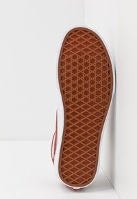 Gummiyttersula med ett diamantmönster i brunt, med vita sidor och en slät kant, som visar upp en lågprofil-sneakerdesign.