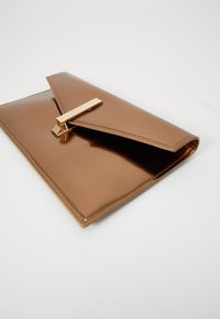 Bronz színű patent bőrből készült clutch táska háromszög alakú fedéllel, arany színű záródással és sima textúrával, tiszta varrással az élek mentén.