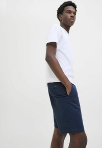 Hvid kortærmet bomulds T-shirt parret med mørkeblå shorts med sidelommer og en knaplukket baglomme, minimal branding.