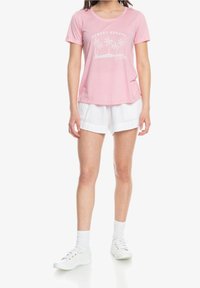 Lyserød t-shirt med korte ærmer og grafik med "SUNSET ESCAPE" samt palmer. Sammen med hvide teksturerede shorts og hvide sneakers. Afslappet pasform.