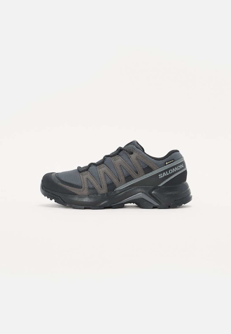 Czarno-szare buty sportowe z siateczkową i syntetyczną cholewką, wyściełanym kołnierzem, teksturowaną podeszwą i kontrastującymi sznurówkami. Widoczne logo po bokach.