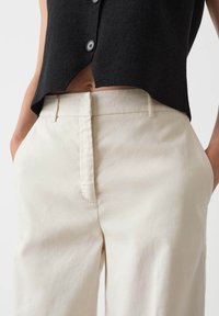 Zwarte getextureerde cropped top met grote knopen, gecombineerd met beigekleurige high-waisted broek van een gladde stof met een voorzak.