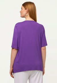 T-shirt viola a maniche corte con vestibilità rilassata, scollo rotondo e spacchi laterali. Tessuto dalla texture liscia, adatto per un abbigliamento casual.