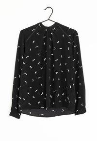 Blouse noire à manches longues avec un nœud au cou, ornée d'un délicat motif de plumes blanches et d'accents texturés le long des épaules.