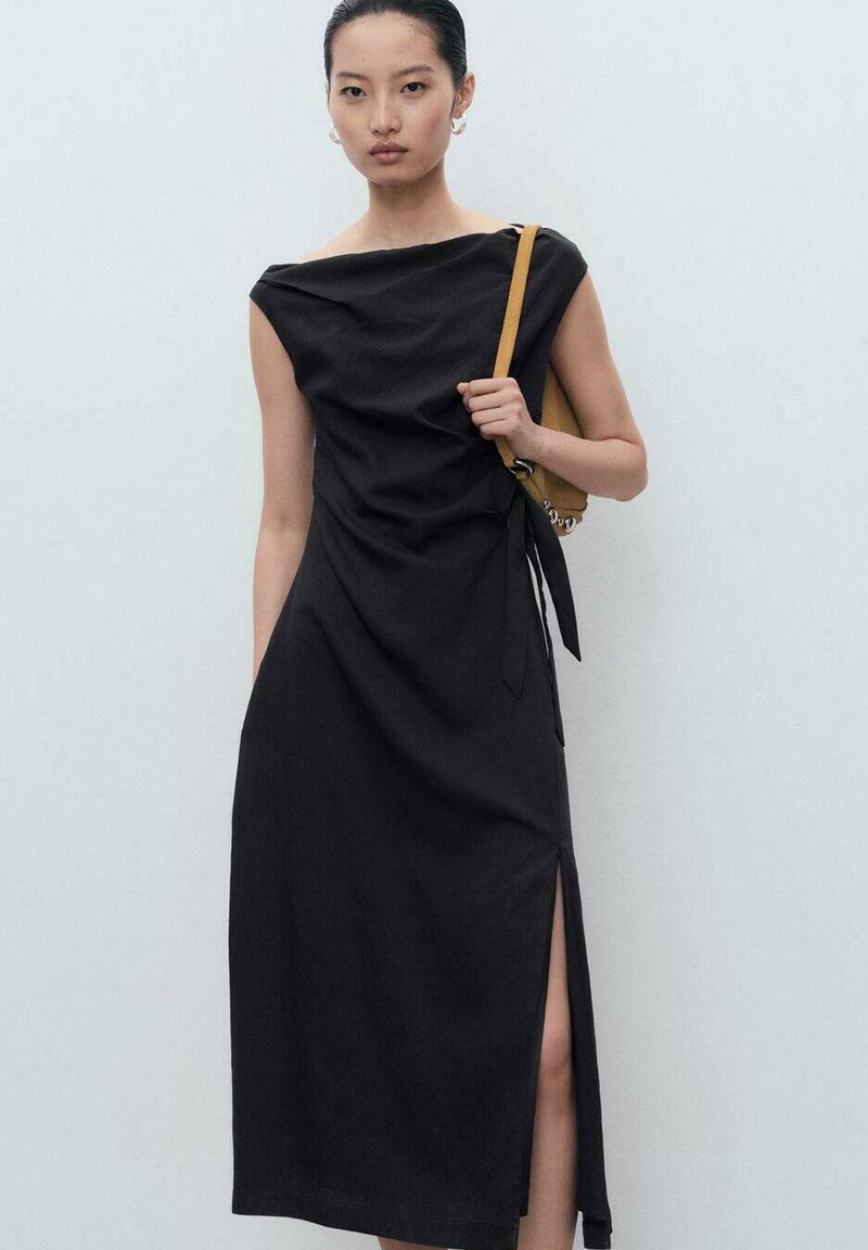 Rochie neagră fără mâneci, cu un design drapat, slit lateral și talie conică. Asortată cu o geantă galbenă, dintr-un material neted și cu detalii minime.