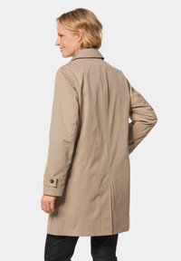 Beige trenchcoat met een col nek, lange mouwen en knoopmanchetten; heeft een rechte snit en een gladde textuur.