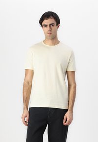 Camiseta de hombre de manga corta en tejido amarillo pálido con cuello redondo. Presenta una textura suave y un ajuste relajado, combinada con unos jeans oscuros.