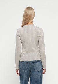 Beige geribbelde trui met lange mouwen en een geschulpte halslijn, gecombineerd met hoge blauwe denim jeans.