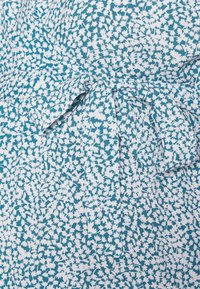 Vestido verde-azulado com um padrão floral branco, apresentando um detalhe de laço na cintura, feito de um tecido leve com uma textura suave.