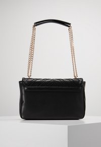 Czarna skórzana torebka z pikowanymi, ukośnymi wzorami z przodu, płaskim dnem i złotymi akcentami na łańcuszku. Posiada zaokrąglony uchwyt u góry.