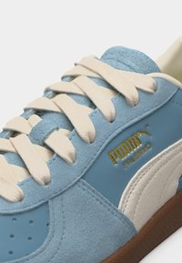 Artimos planas šviesiai mėlynos nubuko Puma Palermo sportbačio su kreminėmis raišteliais ir gumine padais, matyti auksinis Puma logotipas ir balta šoninė juosta.