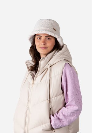 Gilet matelassé crème avec un col haut, associé à une chemise à manches longues texturée de couleur violet clair et un doux chapeau seau blanc.