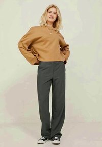 Brown cropped sweatshirt, wide-leg gray trousers, and black sneakers. Smooth texture, relaxed fit, plain design with no visible patterns.