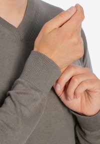 Szary dzianinowy sweter z dekoltem w serek, z prążkowanymi mankietami i gładką fakturą. Ręce dostosowujące rękaw, podkreślające elastyczność tkaniny.