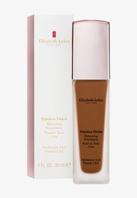 Fond de teint Flawless Finish dans un flacon transparent avec un capuchon en or rose. L'étiquette présente les détails du produit en noir et or sur un fond blanc.