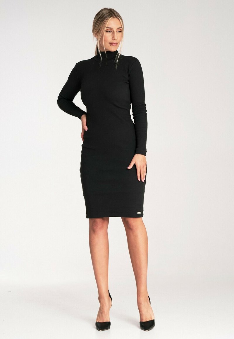 Czarna sukienka bodycon z golfem, długie rękawy, długość do kolan, gładka faktura, dopasowany krój, mały detal z logo na dolnym brzegu, noszona z czarnymi szpilkami.