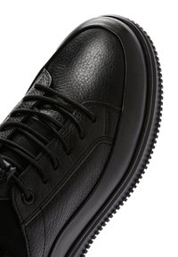 Black leather sneakers featuring a textured upper, round toe, and flat laces. The rubber sole has a tread pattern for grip.