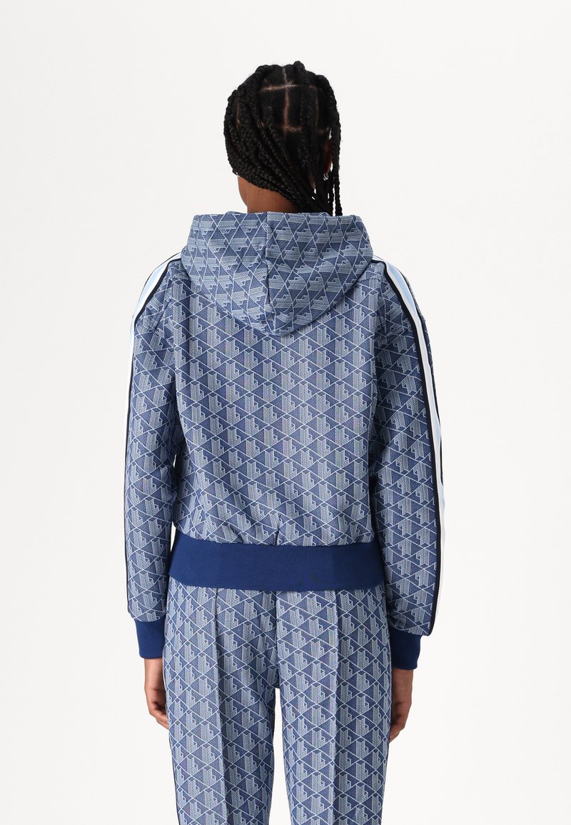 Felpa blu navy con motivo geometrico, cappuccio con cordino e orlo a costine. Accenti bianchi sulle maniche completano il design.