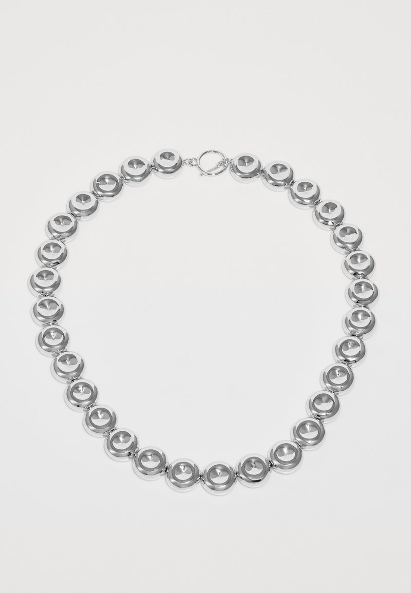 Silvertonad halsband med jämnt fördelade, runda skivpärlor och en togglestängning på en vit bakgrund.