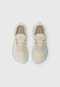 Baskets de sport beiges avec des accents bleu clair, tige texturée et fermeture à lacets. Elles possèdent une semelle souple et un logo proéminent sur la semelle intérieure.