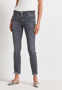 Jeans en denim gris avec une coupe slim, un design à cinq poches, deux boutons à l'avant et des ourlets roulés. Texture lisse avec des détails de décoloration subtile.